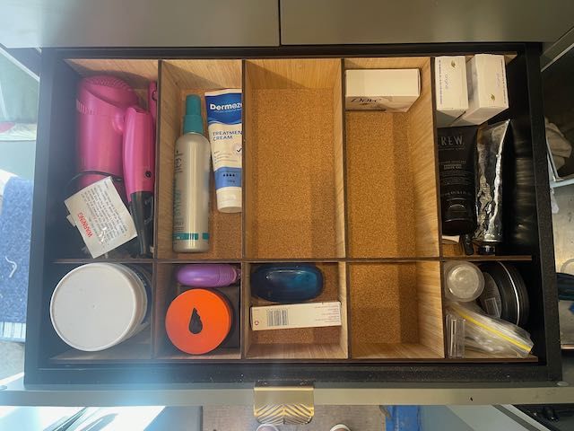 Drawer filled with a variety of bathroom items, including a hair dryer, toothbrush, toothpaste, and shaving cream.